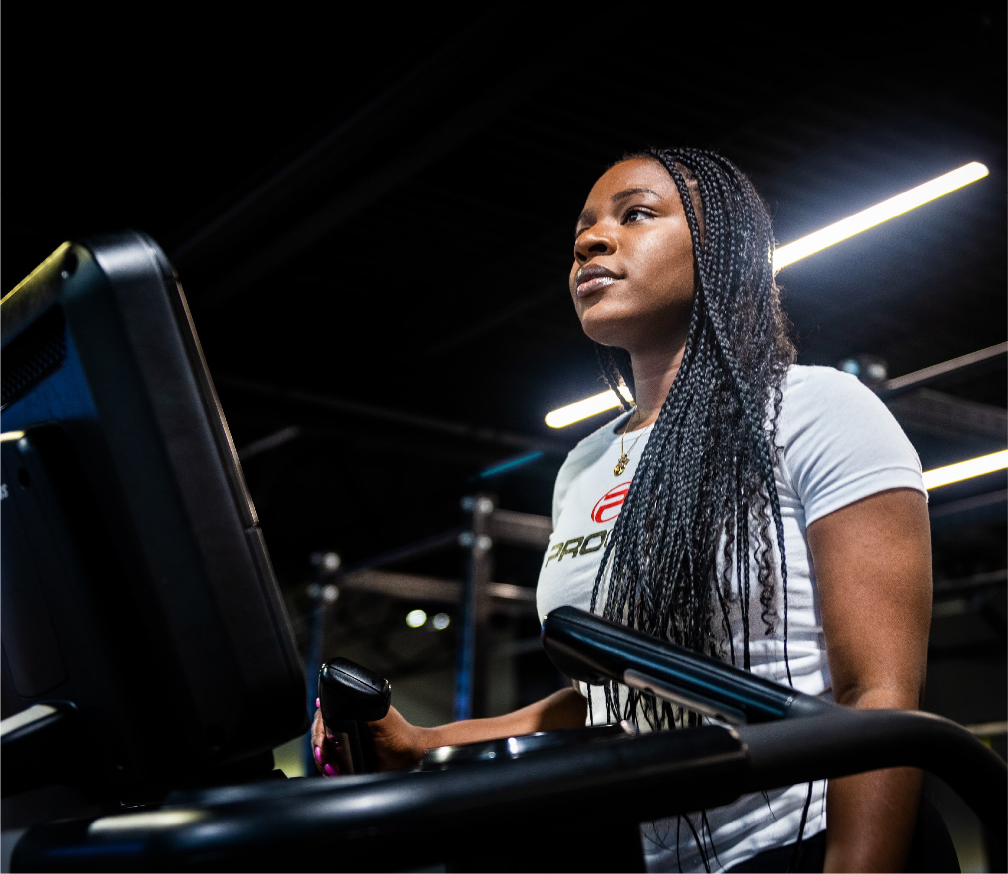 Femme concentrée en plein entraînement sur un tapis roulant, portant un t-shirt blanc ProGym, dans une salle de sport à l’éclairage moderne.