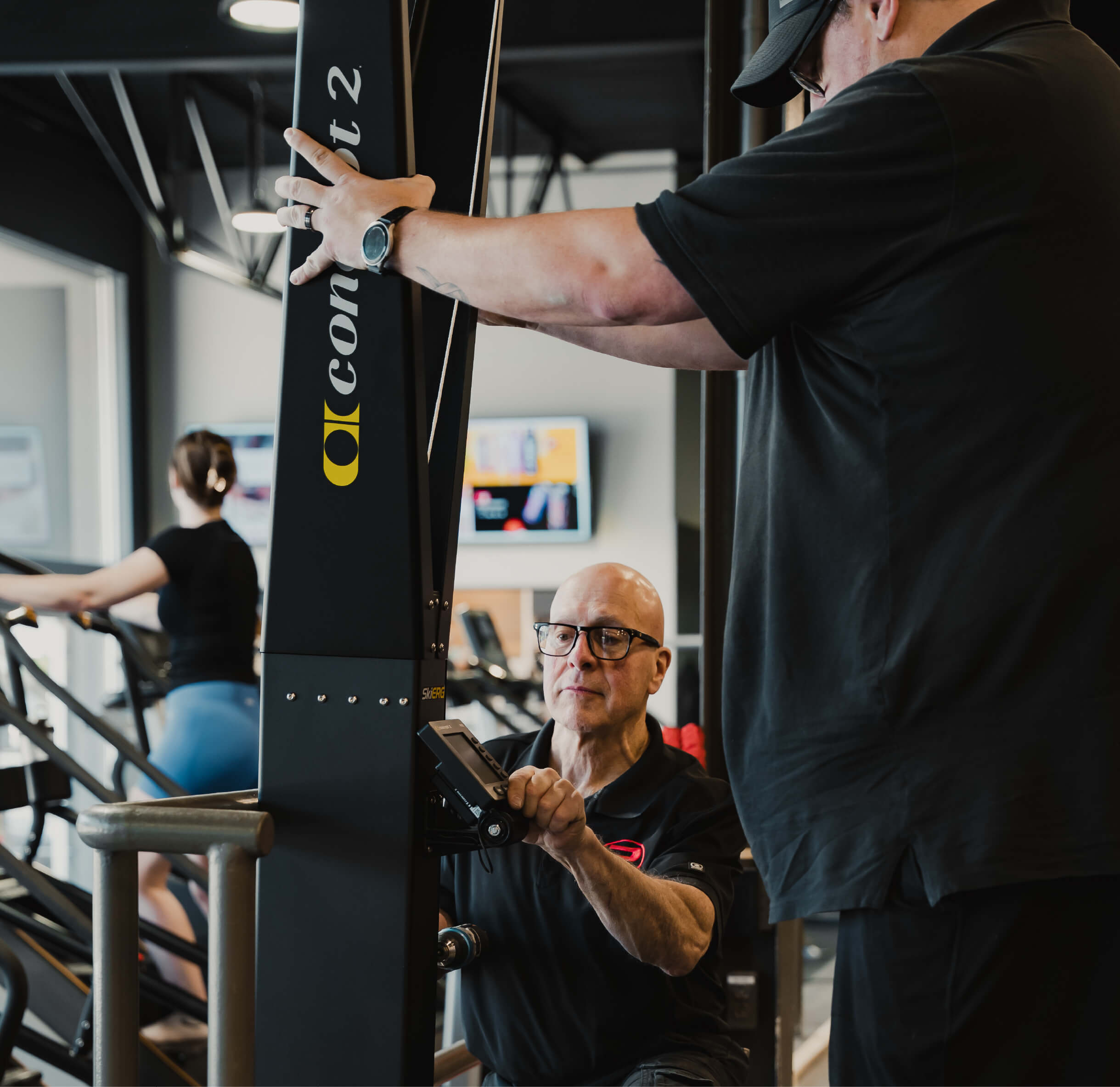 Deux employés de maintenance ajustant une machine d’entraînement dans la salle de musculation.